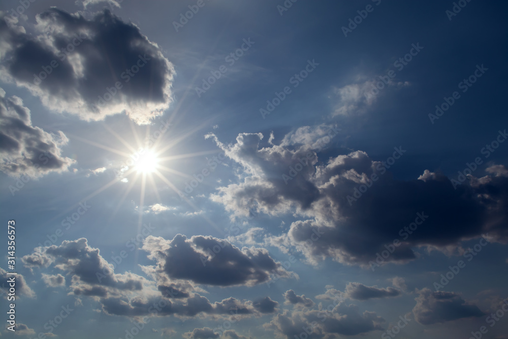 Wall mural sun with rays on a background of blue sky with clouds