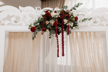Floral composition on the white wedding arch made of eucalyptus and bordeaux flowers