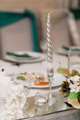Glass candlestick with a silver candle and other decor stuff are on the desk