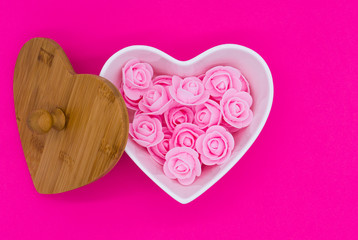 Pink flowers in a heart-shaped casket with wooden lid against a pink background. Valentines day background.