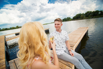 Romantic date surprise. A young guy and a girl on a wooden pier. Raise glasses with champagne.