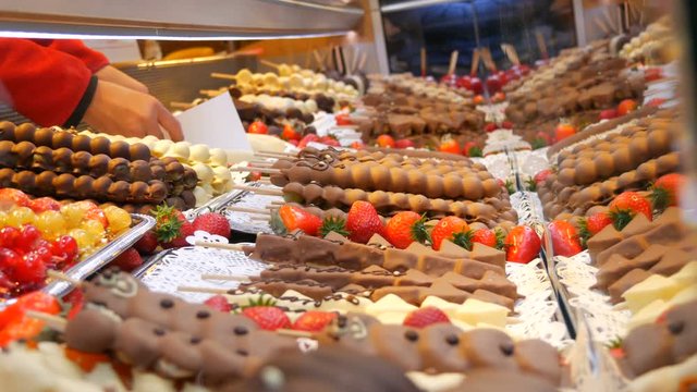 Various fruits on a wooden skewer stick in a caramelized glaze made of milk black white chocolate. Grapes, banana, strawberries in icing on the counter of the Christmas market