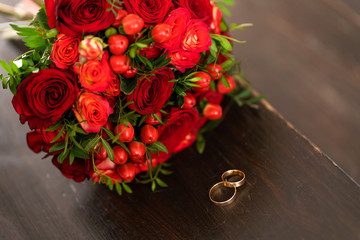 Fototapeta na wymiar Stylish wedding bouquet of red roses next to the wedding rings. Wedding details.