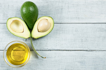 Avocado oil in glass bowl with fresh avocado fruits on white wooden rustic background, Persea americana