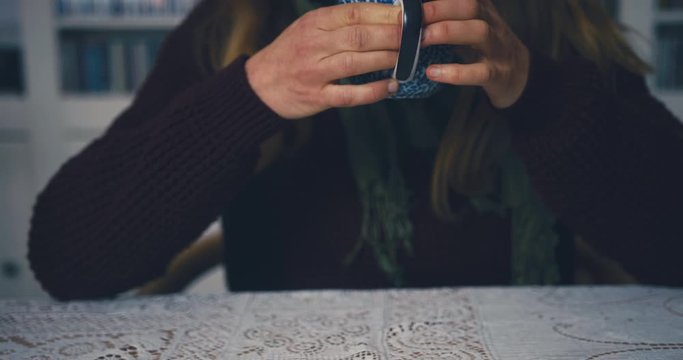 Cold woman with raynaud disease drinking coffee at dining table