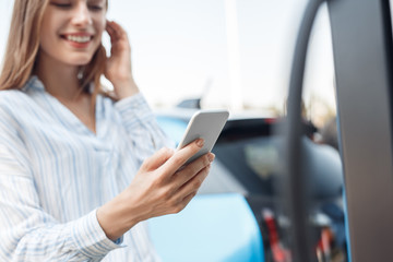 Transportation. Young woman on electric car having stop at charging station using app on smartphone...
