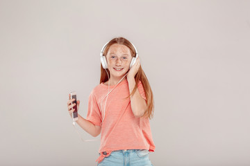 Inclusive Beauty. Girl with freckles in headphones standing isolated on grey holding smartphone listening music smiling playful