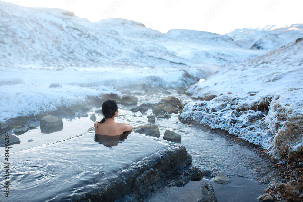 Wall mural the girl bathes in a hot spring in the open air with a gorgeous view of the snowy mountains. incredi