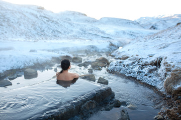 The girl bathes in a hot spring in the open air with a gorgeous view of the snowy mountains. Incredible iceland in winter - obrazy, fototapety, plakaty