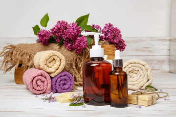 Fototapeta na wymiar Natural cosmetics with lilac flowers. Serum, soap and cream. Face care products. Prepare to bath. Spa therapy concept photo. Organic cosmetic on wooden background. Cosmetics for relax and aromatherapy