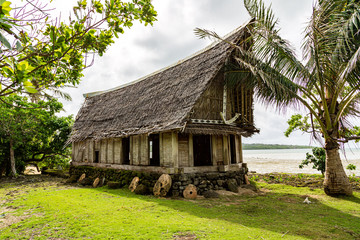 Fototapeta na wymiar Old traditional thatched yapese men's meeting house faluw or fale, on an elevated limestone platform with bank of rai stone money. Shore of South Pacific ocean. Yap island, Micronesia, Oceania