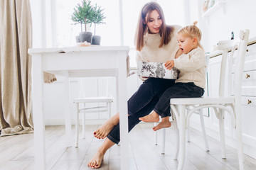 Mother and daughter in a bright kitchen. Homeliness. Joyful baby and his mom. 