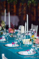 Table setting for a wedding party in pink and turquoise colors. White chairs with silk ribbons. Luxury decor. Plates, glasses, cutlery and candles. Vases with flowers.