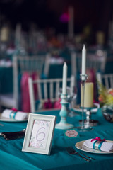 Table setting for a wedding party in pink and turquoise colors. White chairs with silk ribbons. Luxury decor. Plates, glasses, cutlery and candles. Vases with flowers.
