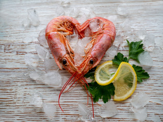 Shrimp in the shape of a heart with a slice of lemon and parsley leaves on old wooden table white color