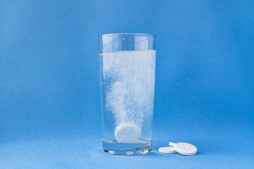 Fizzy aspirin in a glass of water on a blue background. Vertical format and soft focus. - obrazy, fototapety, plakaty