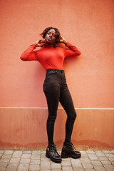 Portrait of a curly haired african woman wearing fashionable red turtleneck posing against rose wall.