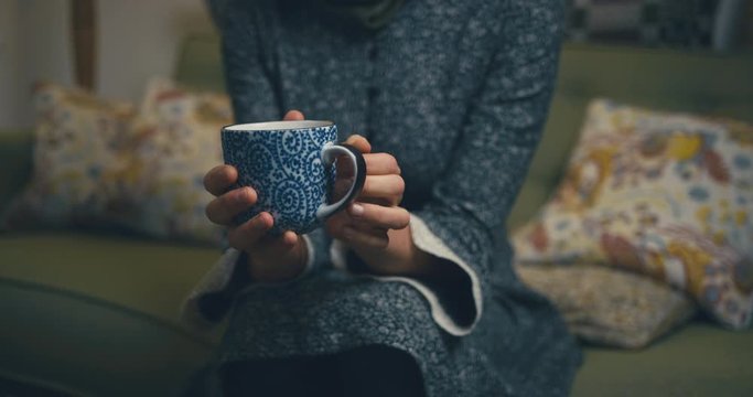 Woman on sofa fidgeting with a cup of coffee