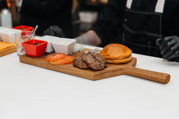The cook is preparing a hamburger, on the background with the ingredients.  Delicious food. Menu, fast food