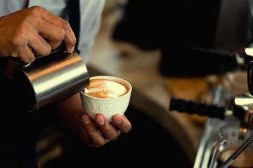 Close-up of male barista hand holding and pouring hot milk for prepare latte art on a green cup of cappuccino coffee. vintage color tone.