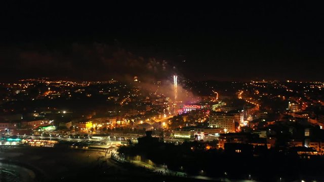 Aerial, pan, drone shot, overlooking fireworks at the coast of Estoril, at night time, New years eve celebration, in Lisbon, Portugal