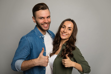 We are happy. Close up photo of a beautiful woman and a handsome man in colorful shirts, who are hugging each other, smiling and showing thumbs up.