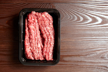 Minced meat. Ground beef in a black plastic tray on wooden table, top view with copy space. Uncooked mincemeat. Fresh raw forcemeat