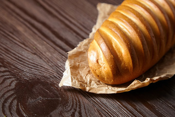 Bakery product. Baked whole bun on wooden table. Loaf, white wheat bread on baking paper on brown background