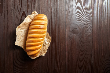 Bakery product. Baked whole bun on wooden table, top view. Loaf, white wheat bread on baking paper on brown background with copy space