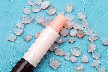 Lip balm with rose quartz stones on a turquoise blue background, grapefruit lipstick macro photography