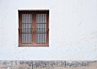 Bleak barred window in a grungy white wall, concept of old abandoned home.