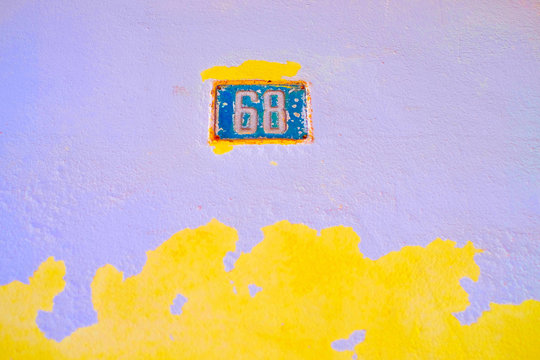 Blue plate number 68, sixty-eight, on a bright wall background with flaking paint showing bright yellow base layer.