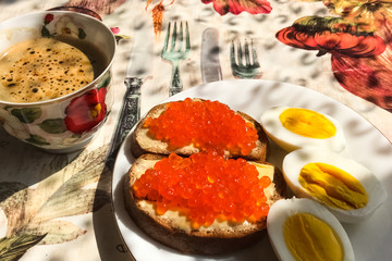 Sandwich with red caviar and boiled eggs, coffee mug. Morning br