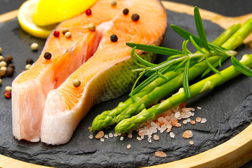 fresh raw salmon steaks with pepper corns, salt, lemon and olive oil on black background. Healthy food, diet concept. Preparation for cooking fish with spices