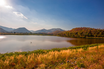 Obraz premium Rozmyte panoramiczne tło przyrody padającego na taflę jeziora słońca, trawy i wiatru wiejącego cały czas wzdłuż wielkich gór, ekologiczne piękno i świeże powietrze.