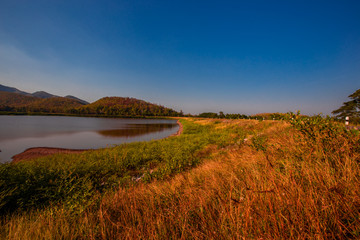 The blurred panoramic nature background of sunlight hitting the lake's surface, grass and wind blowing all the time along the large mountains, ecological beauty and fresh air.