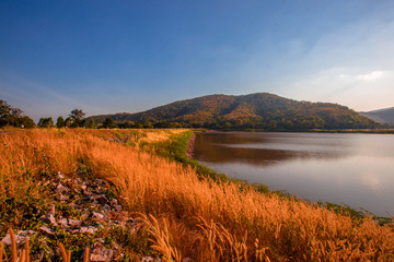 The blurred panoramic nature background of sunlight hitting the lake's surface, grass and wind blowing all the time along the large mountains, ecological beauty and fresh air.