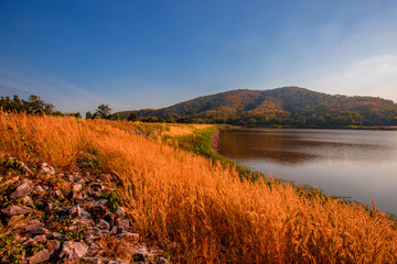 The blurred panoramic nature background of sunlight hitting the lake's surface, grass and wind blowing all the time along the large mountains, ecological beauty and fresh air.