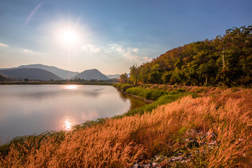 The blurred panoramic nature background of sunlight hitting the lake's surface, grass and wind blowing all the time along the large mountains, ecological beauty and fresh air.