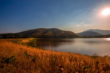 The blurred panoramic nature background of sunlight hitting the lake's surface, grass and wind blowing all the time along the large mountains, ecological beauty and fresh air.