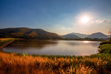 The blurred panoramic nature background of sunlight hitting the lake's surface, grass and wind blowing all the time along the large mountains, ecological beauty and fresh air.