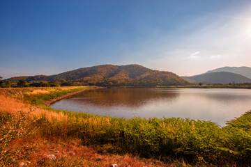 The blurred panoramic nature background of sunlight hitting the lake's surface, grass and wind blowing all the time along the large mountains, ecological beauty and fresh air.