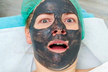 Young woman in a beauty salon with a black mask on her face. The concept of cosmetology. The...
