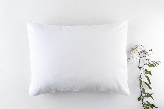 Blank white pillow on an off-white background with white flowers and baby boots - flat lay pillowcase mockup