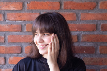 Portrait of a beautiful brunette woman with bangs wearing a black t-shirt who is happy and smiling on brick wall background