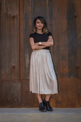 portrait of a beautiful latin woman with shirt, white skirt and folded arms in rusty iron background