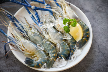 Raw shrimps on white plate - fresh shrimp prawns with ice and spices lemon for cooking on dark background in the seafood restaurant