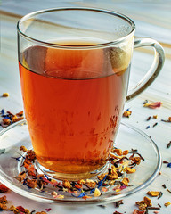 Red fruit tea in a tea glass, on a glass saucer. Surrounded by colorful dried tea leaves. Close-up. Isolated on white marble as a backdop. Tabletop.