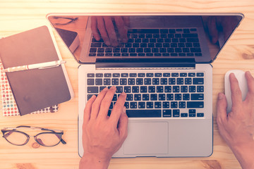 A man is working by using a laptop computer on vintage wooden table. Hands typing on a keyboard. Top view.
