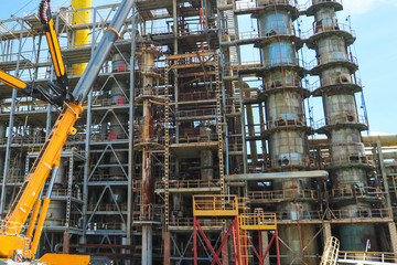 Construction and installation work with a powerful construction crane of a large new industrial oil refining petrochemical chemical plant with pipes, columns, railings, stairs and equipment